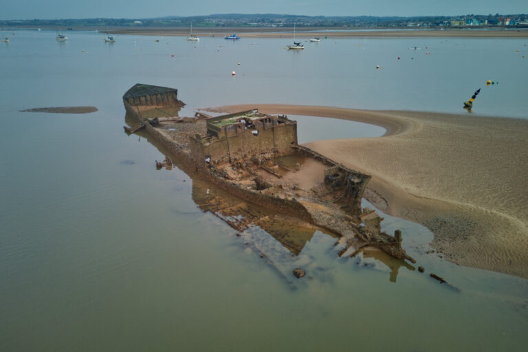 Aerial view of the wreck of the South Coaster, a partially submerged and decaying shipwreck in the Exe River near Starcross and Exeter. The surrounding sandbanks boats add to the maritime atmosphere.